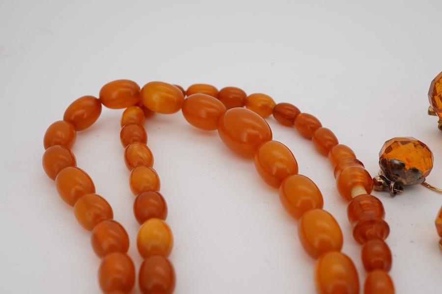 A single strand graduated oval amber bead necklace, 40cm, gross weight 9 grams, together with an amber cluster set brooch and pair of earrings.